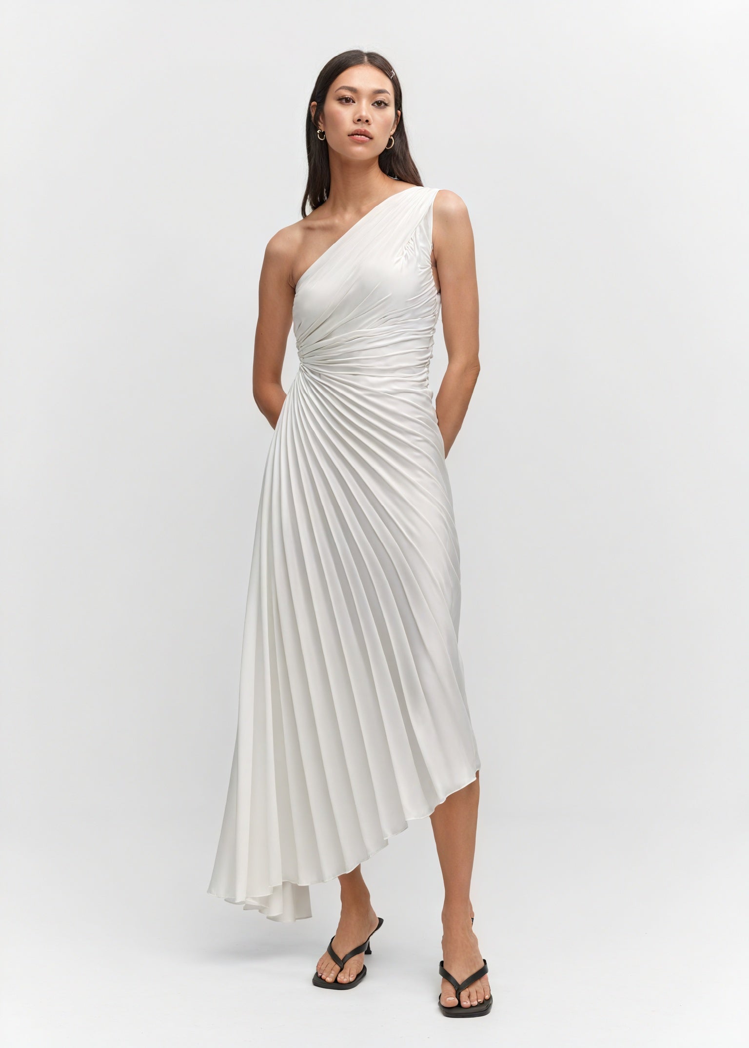 Light pink monospalla pleated dress with asymmetric hem by Montaracrest, featuring a sleek, elegant design and flowing fabric.