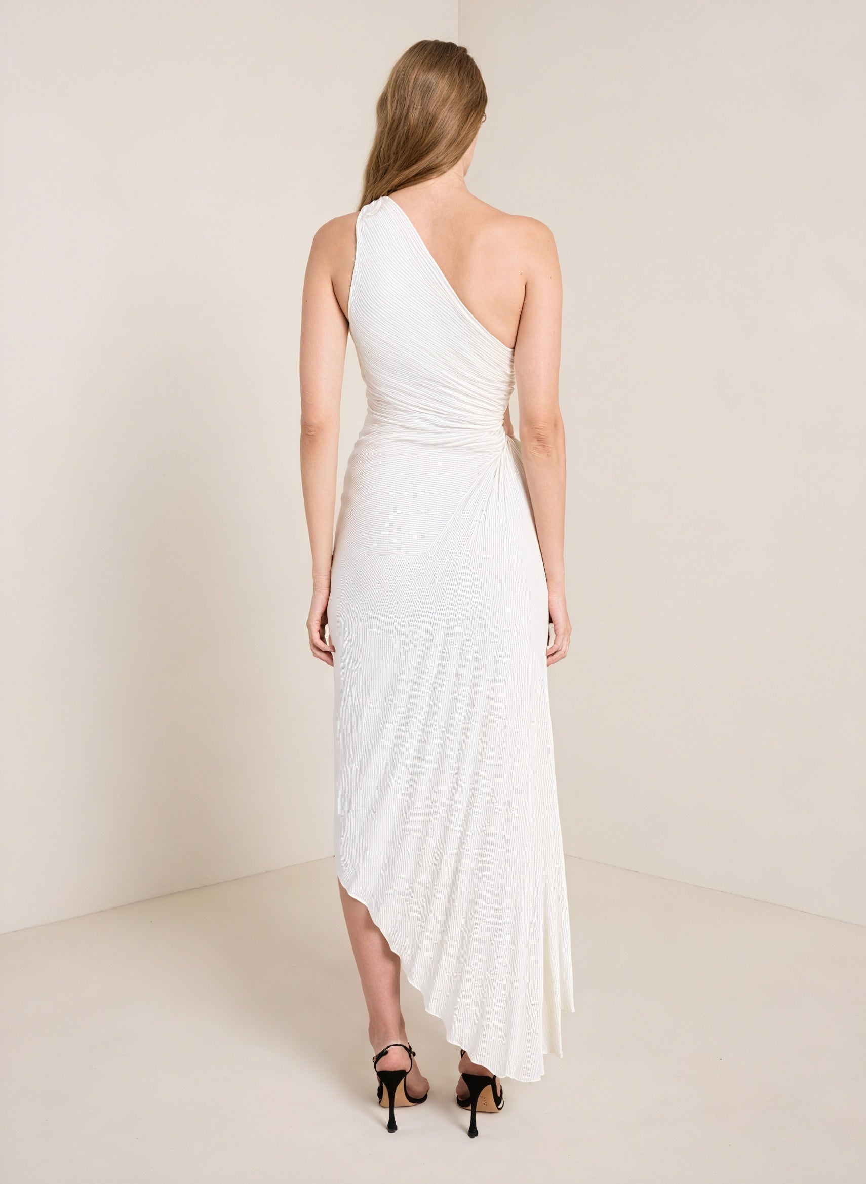 Cream monospalla pleated dress with asymmetric hem by Montaracrest, featuring a stylish one-shoulder design and flowing fabric.